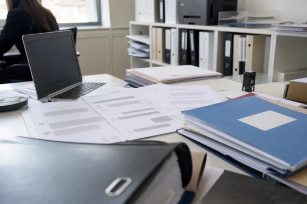 Feuilles imprimées de conversations Messenger, ordinateur ouvert et dossiers de procédure dans un cabinet de commissaire de justice.