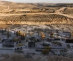 Vue plongeante d’un chantier E1 en Cisjordanie, avec terrassements, engins, talus de terre et collines basses au fond.