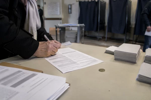 Une charte papier, un stylo et une pièce d’un euro sur une table, devant des isoloirs et des bulletins vierges.