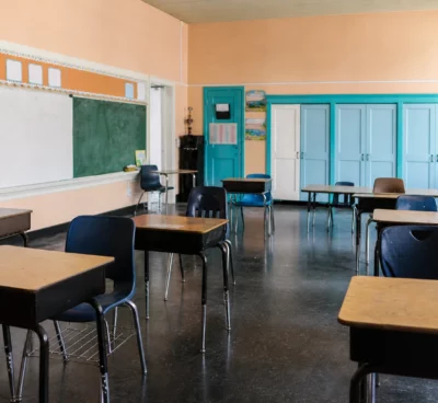 Salle de classe française vide avec bureaux d’élèves, tableau, portes turquoise et lumière du jour froide.