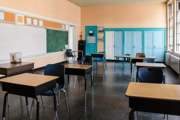 Salle de classe française vide avec bureaux d’élèves, tableau, portes turquoise et lumière du jour froide.