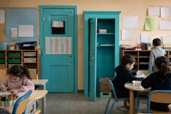Classe de maternelle française en usage, tables d’enfants, mobilier usé, affichages neutres et lumière douce