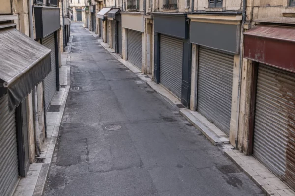Rue commerçante française bordée de boutiques fermées, leurs rideaux métalliques baissés le long d’un trottoir usé.
