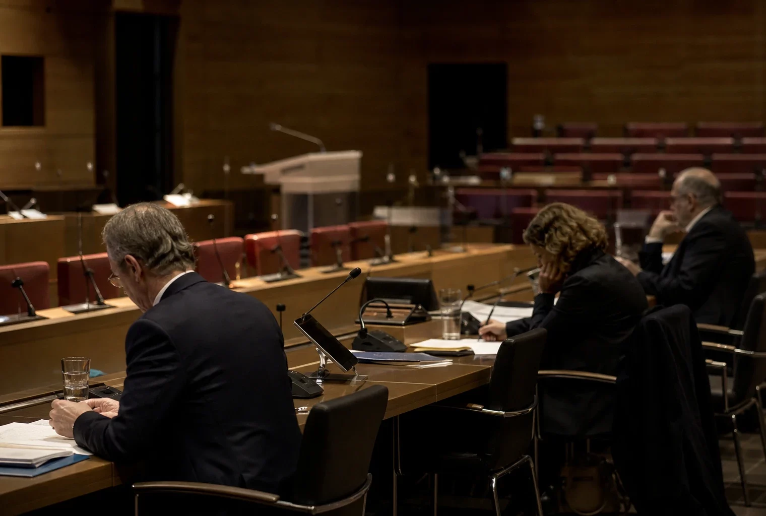 Salle de commission à l’Assemblée nationale, tables alignées, micros et dossiers, quelques élus espacés sous lumière chaude du soir.