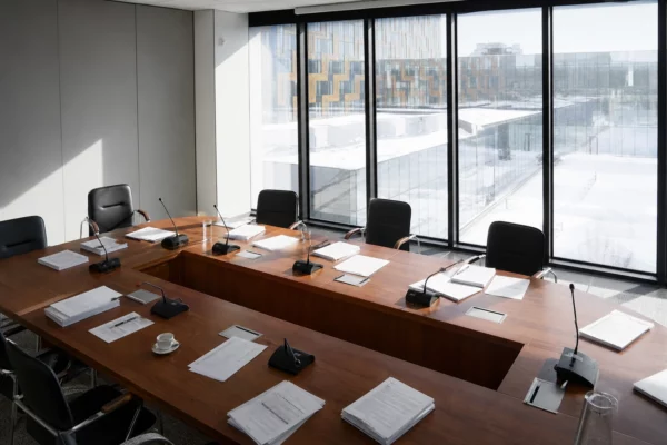 Salle du Conseil des ministres vide, grande table de réunion, dossiers budgétaires, micros et chaises sous une lumière matinale.
