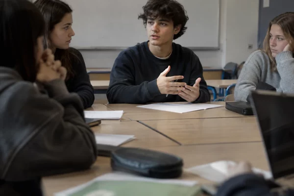 Salle de lycée préparée pour une réunion, avec des chaises scolaires autour d’une table et un tableau mural en arrière-plan.