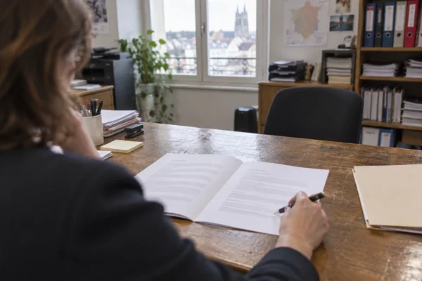 Contrat de travail ouvert sur un bureau usé, avec stylo et dossier papier, dans une permanence parlementaire aux rayonnages chargés.
