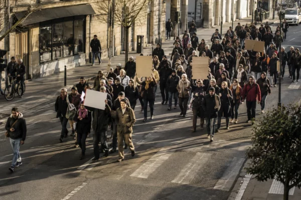 Un groupe de manifestants marche dans une rue de ville, quelques pancartes sans texte se détachant des façades.