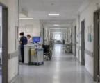 Un couloir d’hôpital en activité, avec un chariot de soins et un fauteuil roulant près du poste de soins.