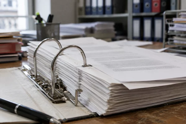 Un dossier administratif ouvert sur un bureau de traitement, avec des feuillets vierges et du matériel de classement en arrière-plan.