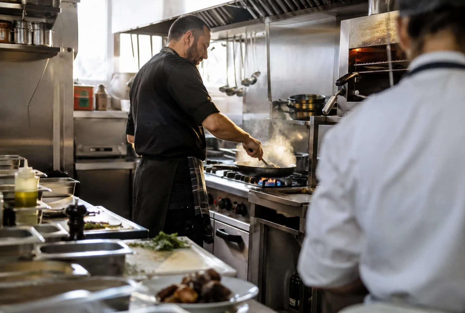 Une personne prépare un plat dans une cuisine de restaurant équipée de plans de travail en inox et de matériel professionnel.