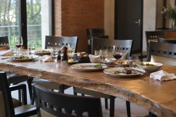 Table en bois marquée, dressée pour un déjeuner terminé, avec assiettes entamées et chaises vides dans une salle de restaurant.