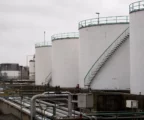 Dépôt pétrolier français avec cuves métalliques blanches, passerelles vertes et tuyaux techniques sous ciel couvert.