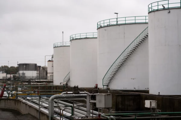 Dépôt pétrolier français avec cuves métalliques blanches, passerelles vertes et tuyaux techniques sous ciel couvert.