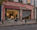 Devanture de commerce aux vitrines brisées et au rideau métallique abîmé, avec des éclats de verre sur le trottoir.