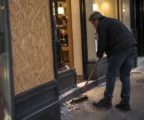 Devanture d’un commerce avec une vitre remplacée par un panneau et quelques débris balayés près de l’entrée.