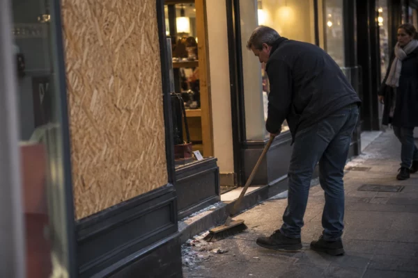 Devanture d’un commerce avec une vitre remplacée par un panneau et quelques débris balayés près de l’entrée.