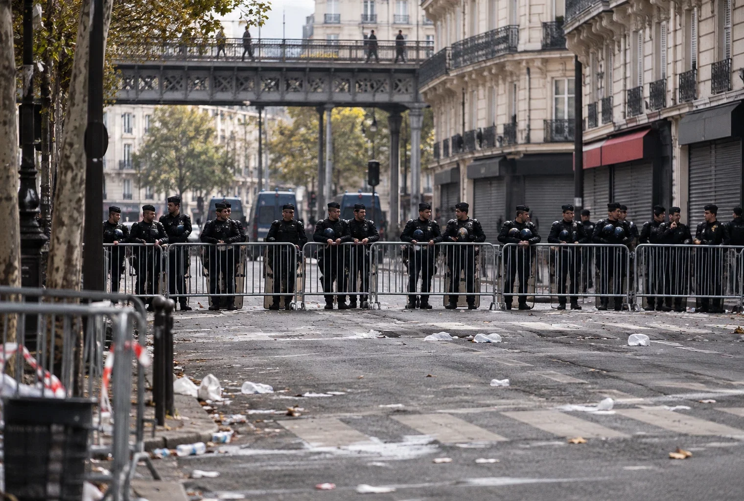Policiers et gendarmes derrière des barrières métalliques dans une rue parisienne, alors que la chaussée se dégage.