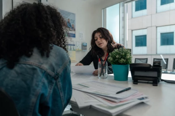 Guichet CAF lumineux avec dossier APL étudiant, formulaires et dossiers papier sur le comptoir, ambiance administrative réelle.