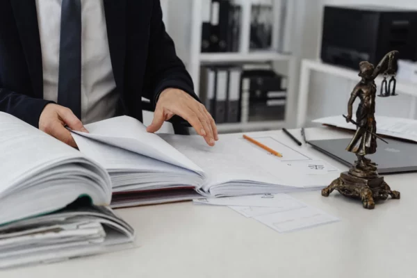 Mains d’huissier sur un dossier ouvert, feuilles imprimées et ordinateur dans un bureau sobre en France.