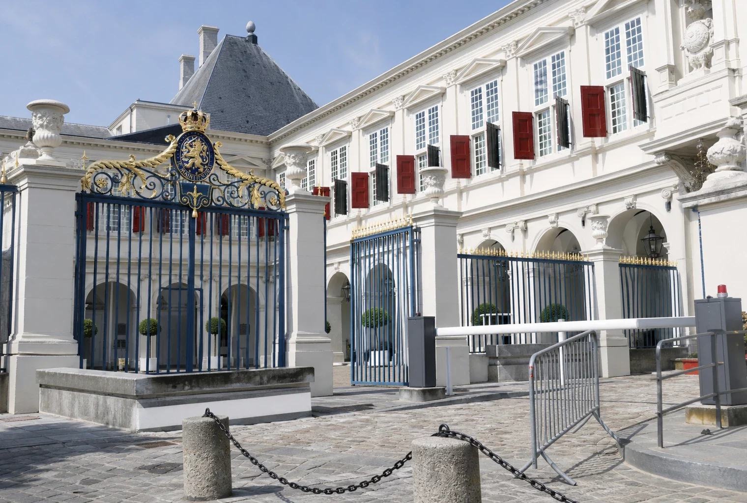 Grille de l’Élysée et façade blanche du palais en cour intérieure, sous un soleil de fin de matinée, sans drapeau ni texte.