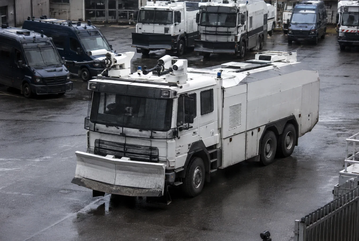 Un véhicule lanceur d’eau de la police stationne dans une cour avec d’autres véhicules d’intervention en arrière-plan.