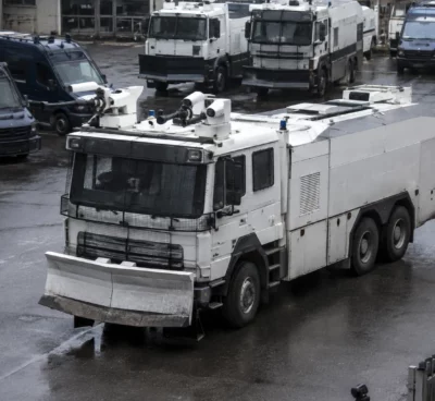 Un véhicule lanceur d’eau de la police stationne dans une cour avec d’autres véhicules d’intervention en arrière-plan.