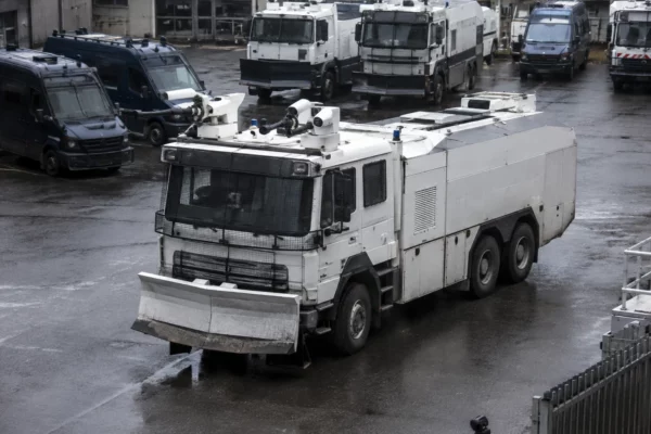 Un véhicule lanceur d’eau de la police stationne dans une cour avec d’autres véhicules d’intervention en arrière-plan.