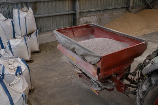 Granulés d’engrais phosphaté près de la trémie d’un épandeur, dans un hangar agricole aux structures métalliques