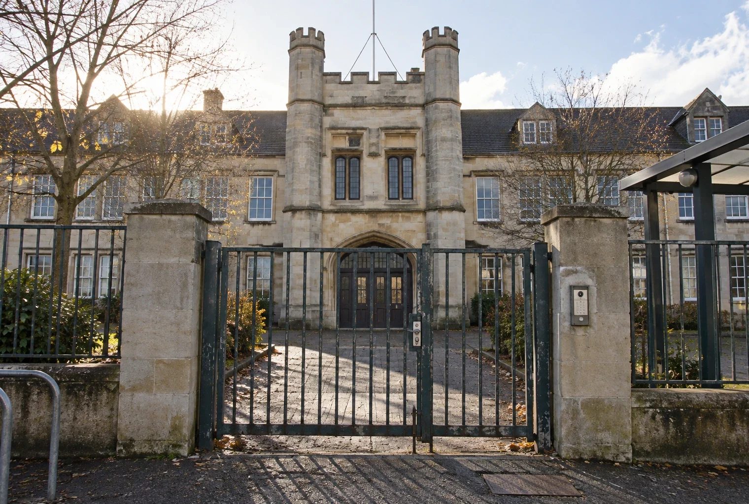 Portail métallique devant l’entrée d’une école, avec une façade scolaire et des fenêtres visibles au fond, sans inscription lisible.