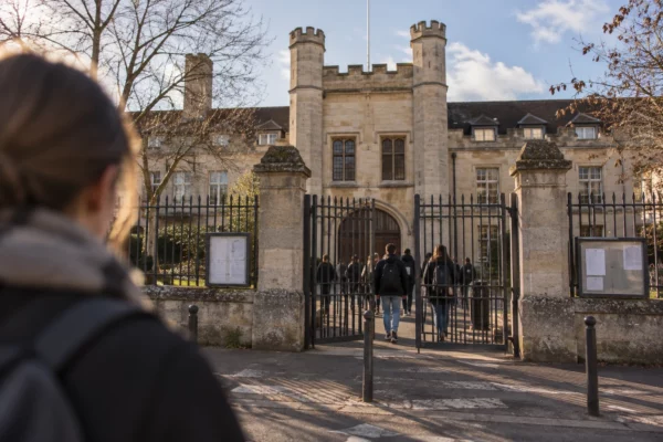 Entrée d’un lycée français avec portail métallique et clôture devant une façade de pierre, dans la lumière basse d’hiver.