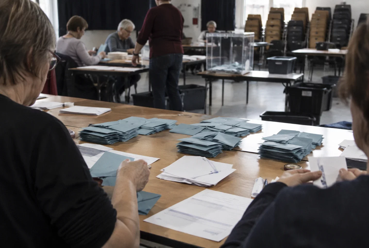 Des enveloppes électorales ouvertes et regroupées sur une table, avec des feuilles de comptage et des bacs de tri en arrière-plan.