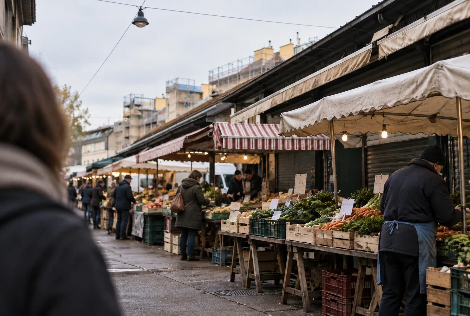 Étalages démontables, cagettes et auvents usés s’alignent dans une allée de marché de plein air bordée de façades.