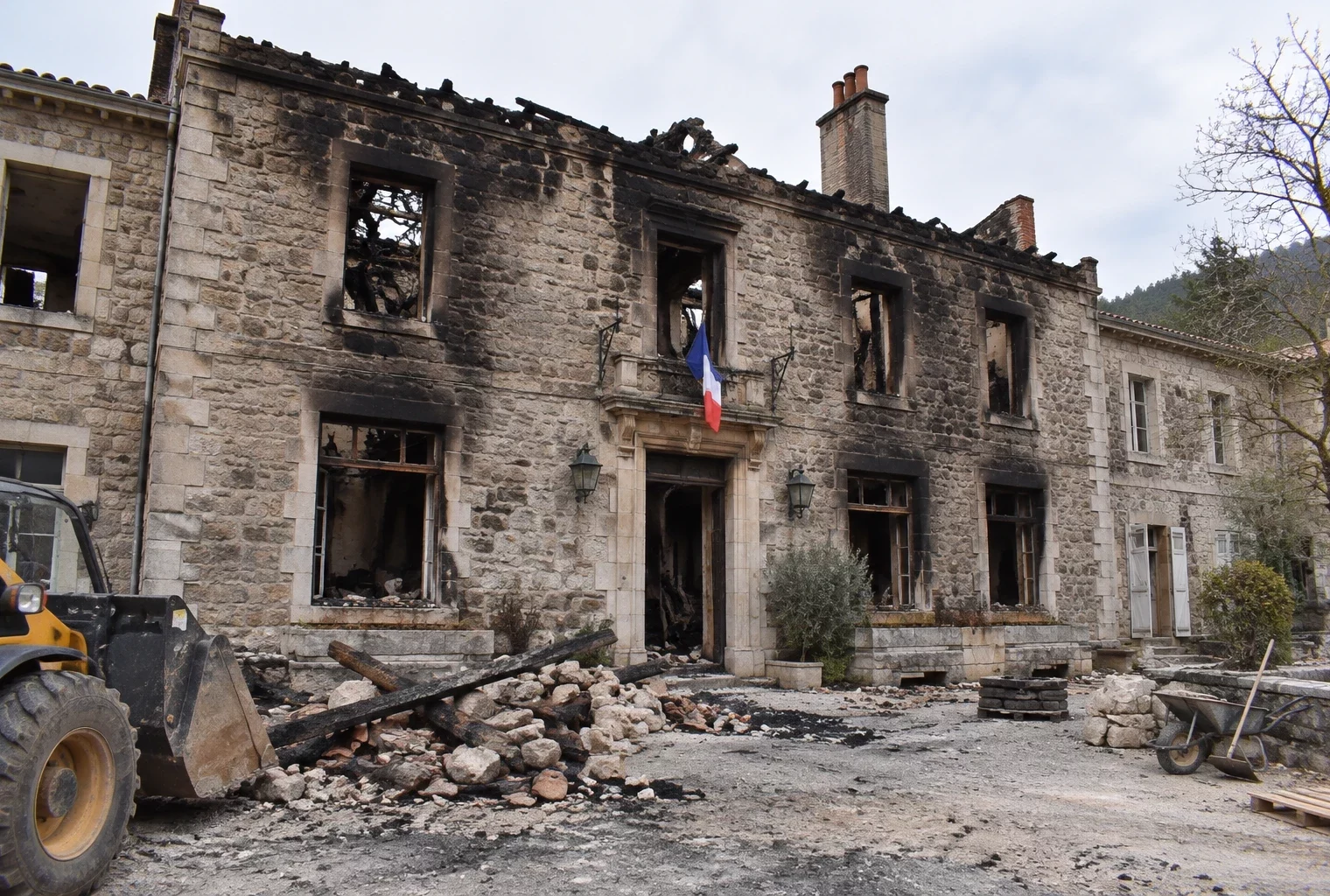 Façade municipale ancienne noircie par un incendie, avec fenêtres endommagées et débris dispersés au pied du bâtiment.