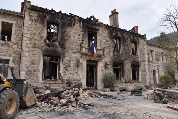 Façade municipale ancienne noircie par un incendie, avec fenêtres endommagées et débris dispersés au pied du bâtiment.