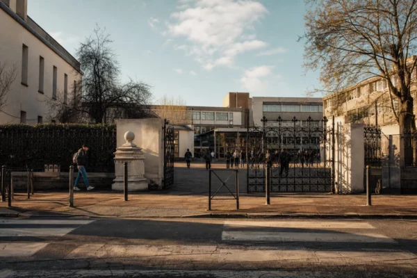 Grilles du lycée Auguste-Béhal à Lens au soleil bas, façade en arrière-plan et rue vide devant l’entrée.