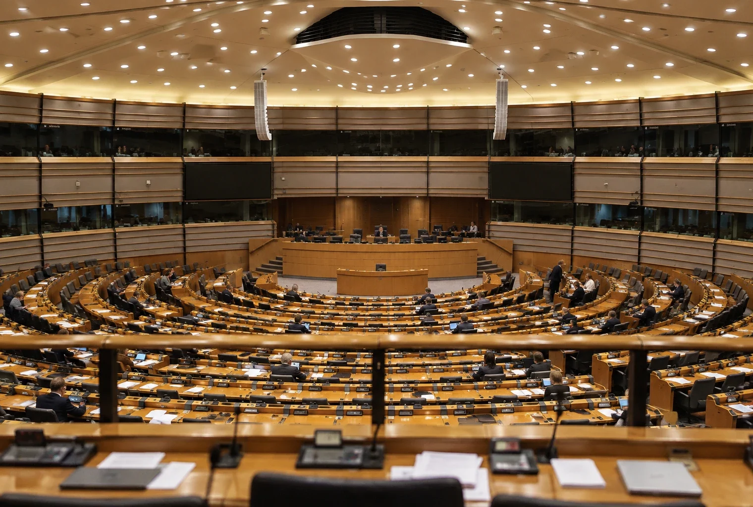 Rangées de pupitres en bois équipés de microphones et de boîtiers de vote dans un hémicycle parlementaire éclairé le soir.