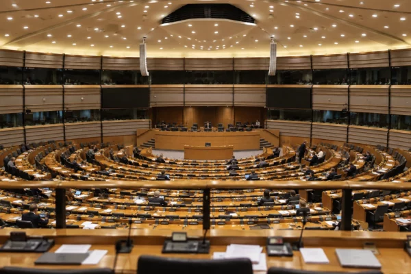 Rangées de pupitres en bois équipés de microphones et de boîtiers de vote dans un hémicycle parlementaire éclairé le soir.