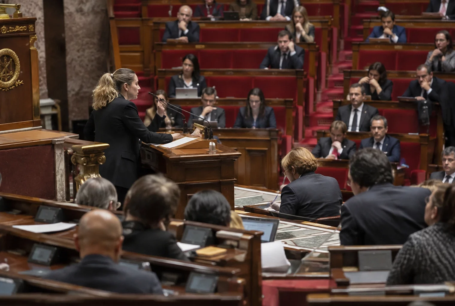 Pupitres équipés de microphones et de consoles de vote dans un hémicycle parlementaire aux rangées de sièges visibles.
