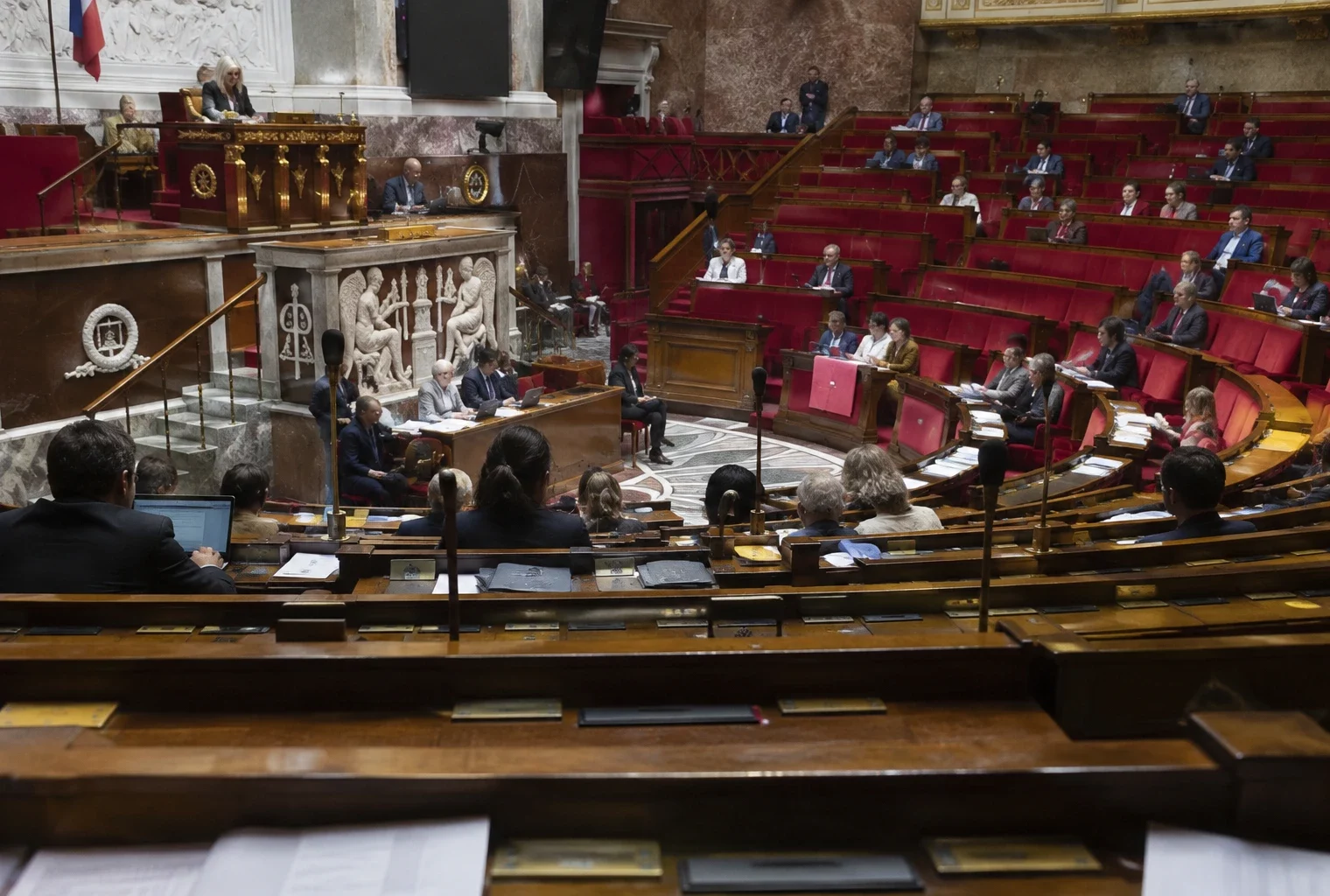 Rangées de pupitres équipés de microphones et de boîtiers de vote dans un hémicycle parlementaire.