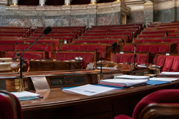 Pupitres équipés de microphones et documents budgétaires dans un hémicycle parlementaire aux rangées de sièges.