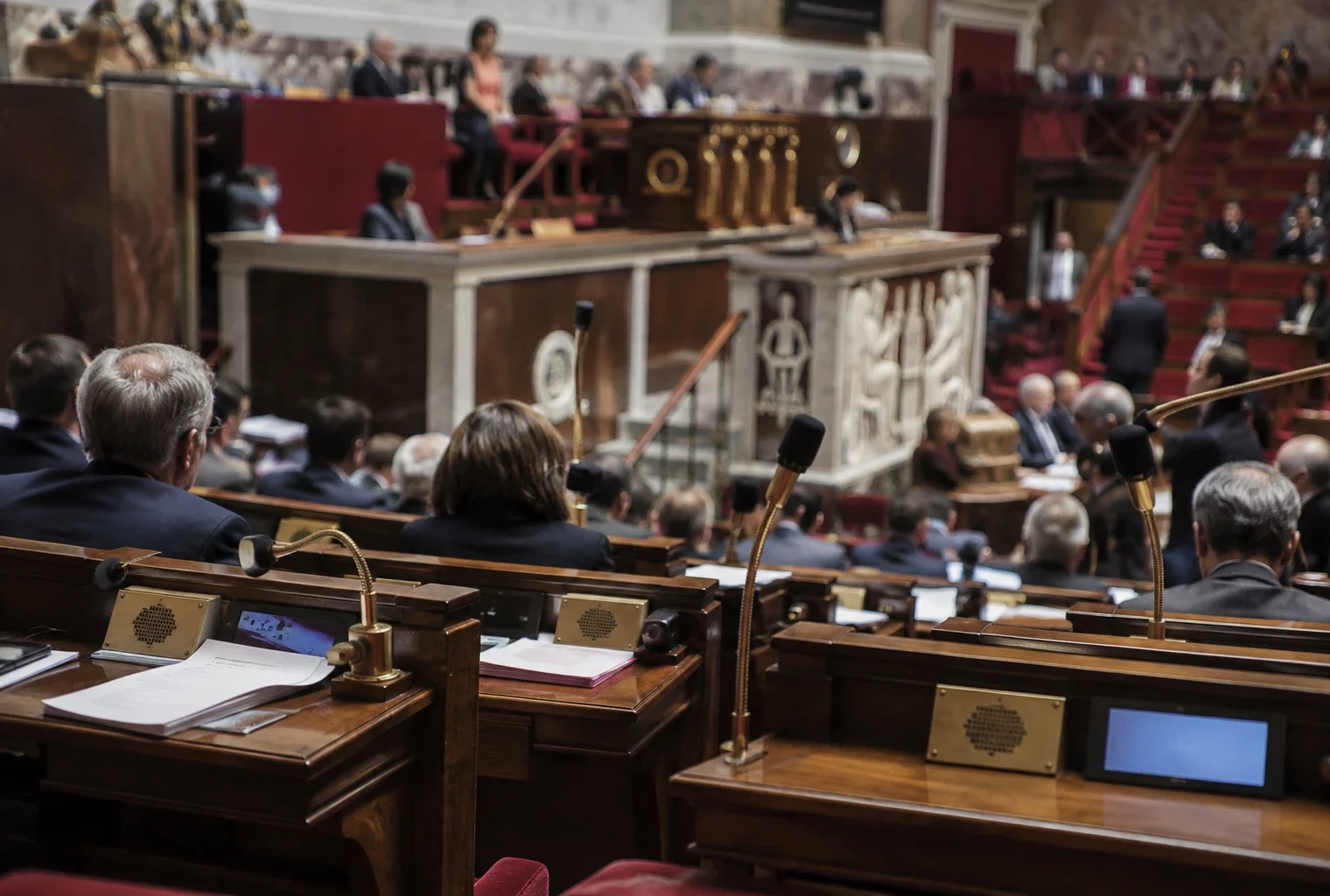 Pupitres équipés de microphones et de boîtiers de vote dans un hémicycle parlementaire aux rangées de sièges incurvées.