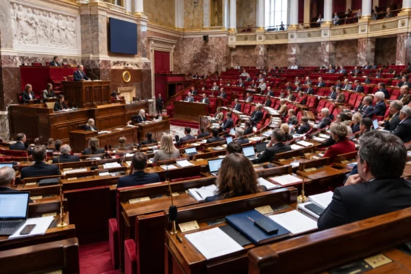 Vue large de l’hémicycle, avec ses rangées de pupitres en bois, microphones, consoles de vote et sièges rouges.