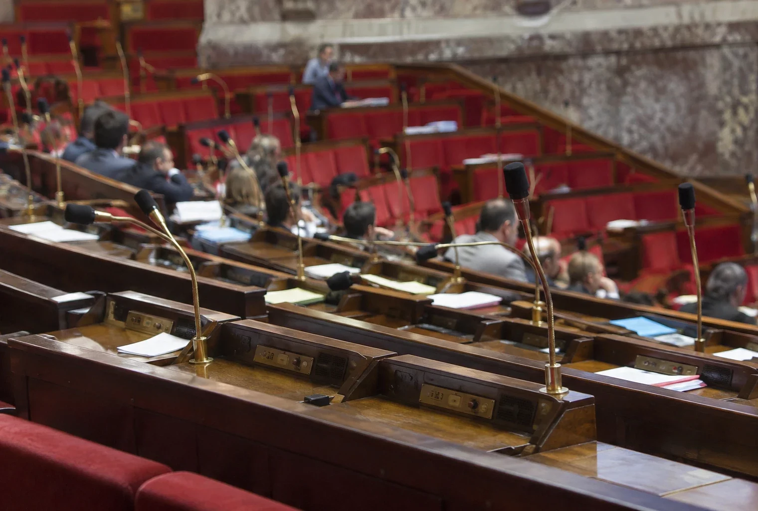 Pupitres équipés de microphones et de boîtiers de vote dans un hémicycle parlementaire aux rangées de sièges courbes.