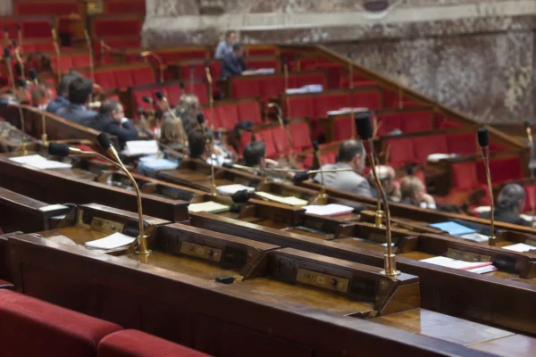 Pupitres équipés de microphones et de boîtiers de vote dans un hémicycle parlementaire aux rangées de sièges courbes.