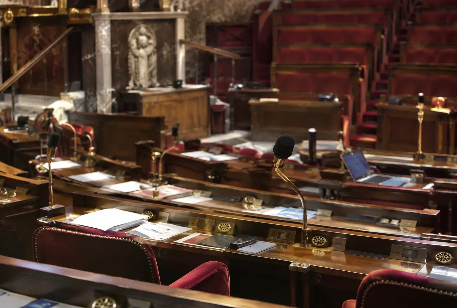 Pupitres équipés de microphones et de boîtiers de vote disposés en rangées dans un hémicycle parlementaire vide.
