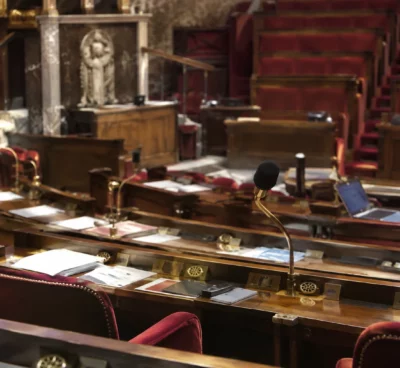 Pupitres équipés de microphones et de boîtiers de vote disposés en rangées dans un hémicycle parlementaire vide.