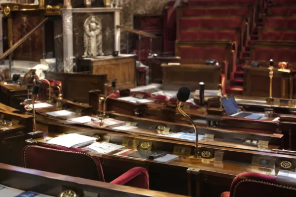 Pupitres équipés de microphones et de boîtiers de vote disposés en rangées dans un hémicycle parlementaire vide.