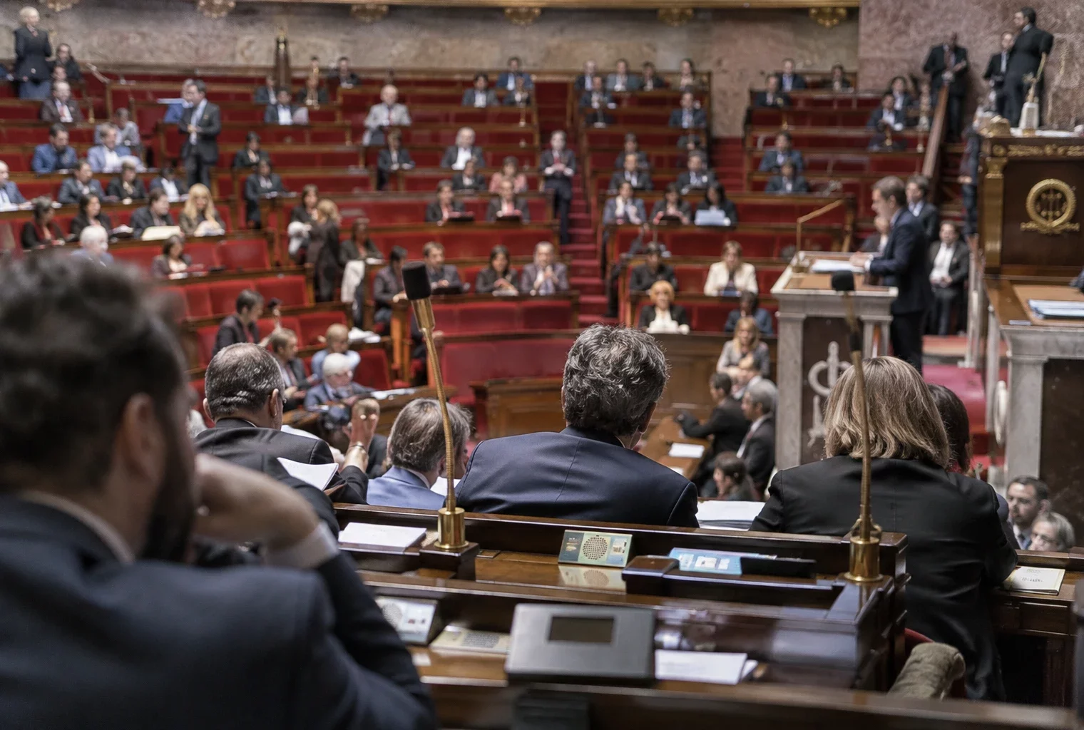 Pupitres équipés de microphones et de boîtiers de vote dans un hémicycle parlementaire aux sièges disposés en arc.