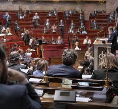 Pupitres équipés de microphones et de boîtiers de vote dans un hémicycle parlementaire aux sièges disposés en arc.